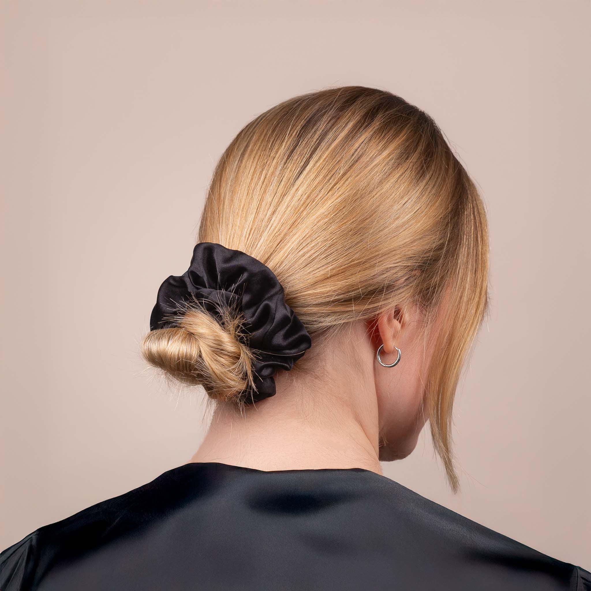 Side view of the Large Silk Scrunchie in Black securing hair in a low bun, showing its soft sheen and gentle drape.