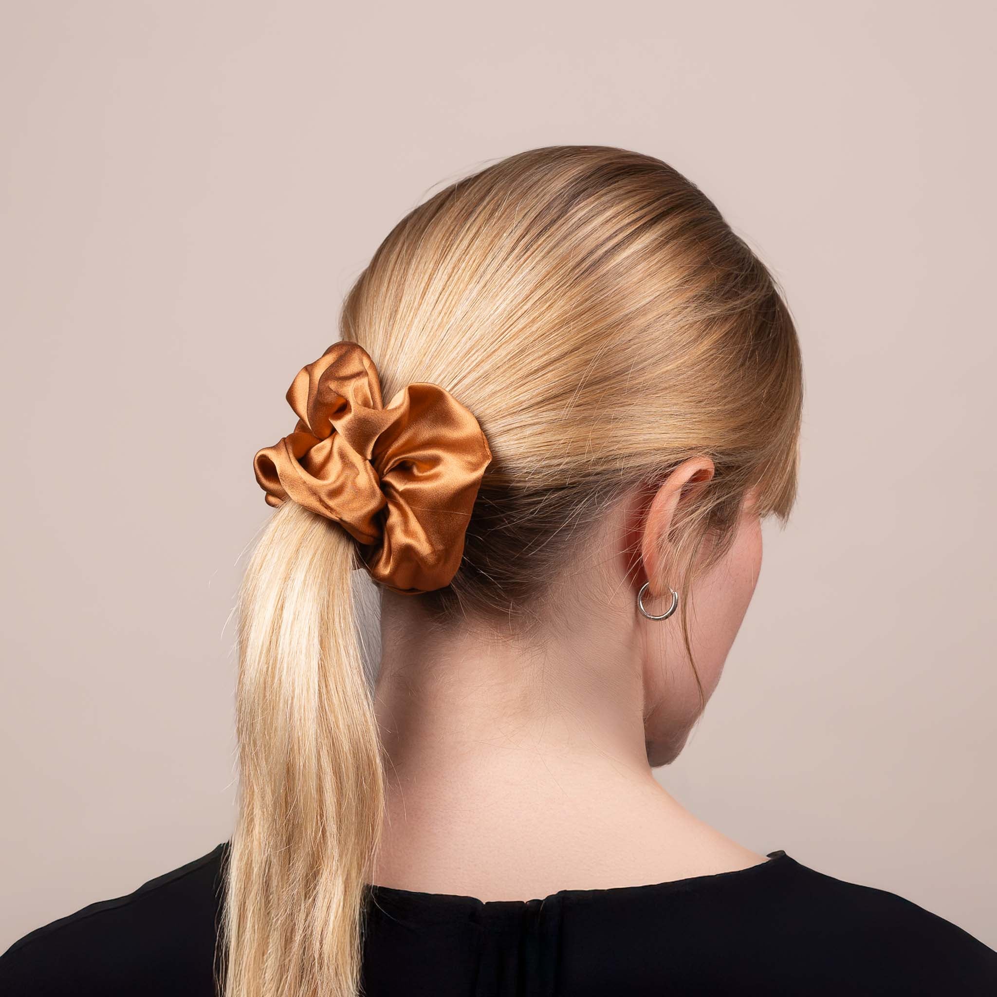 Side view of the Large Silk Scrunchie in Caramel Brown securing hair in a low ponytail, with a soft sheen and drape.