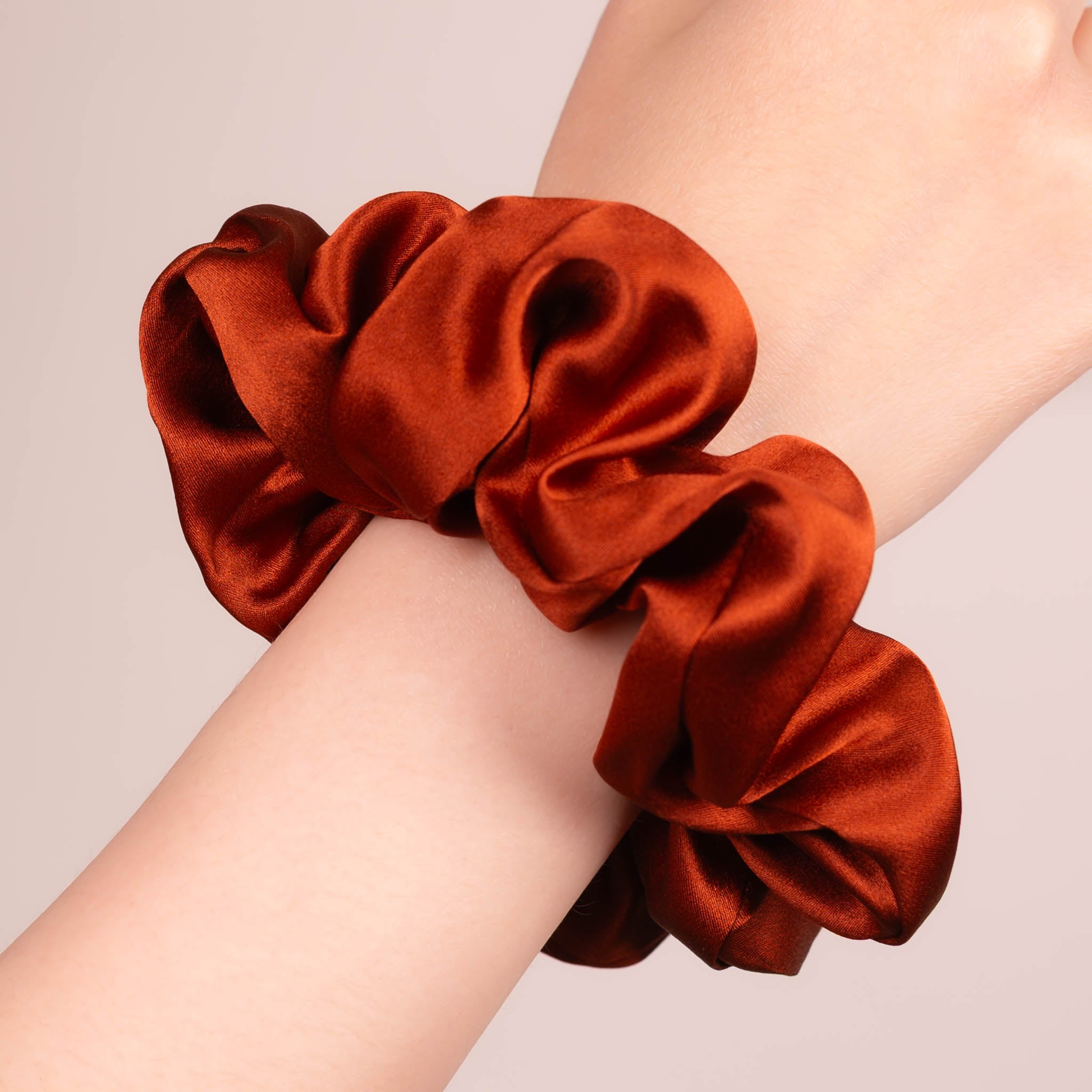 Large Silk Scrunchie in Deep Terracotta—a vibrant orange red —worn on a wrist, showing a natural soft sheen and gentle drape.