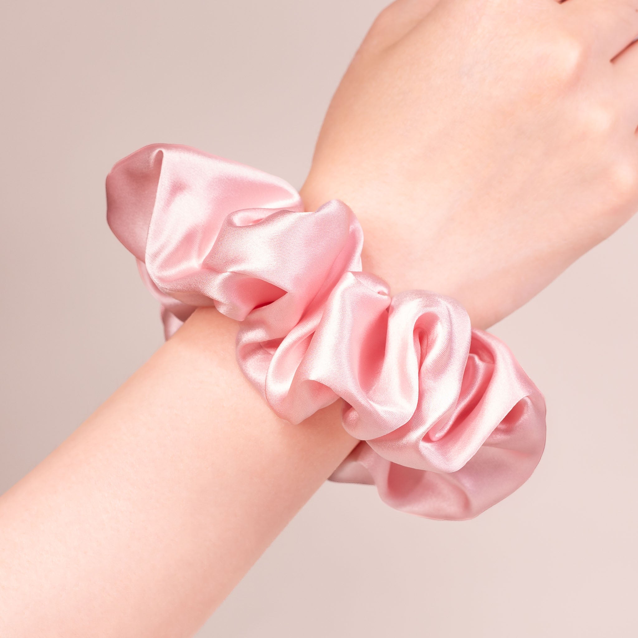 Large Silk Scrunchie in Peony Pink—a light peachy pink—worn on a wrist, showing a natural soft sheen and gentle drape.
