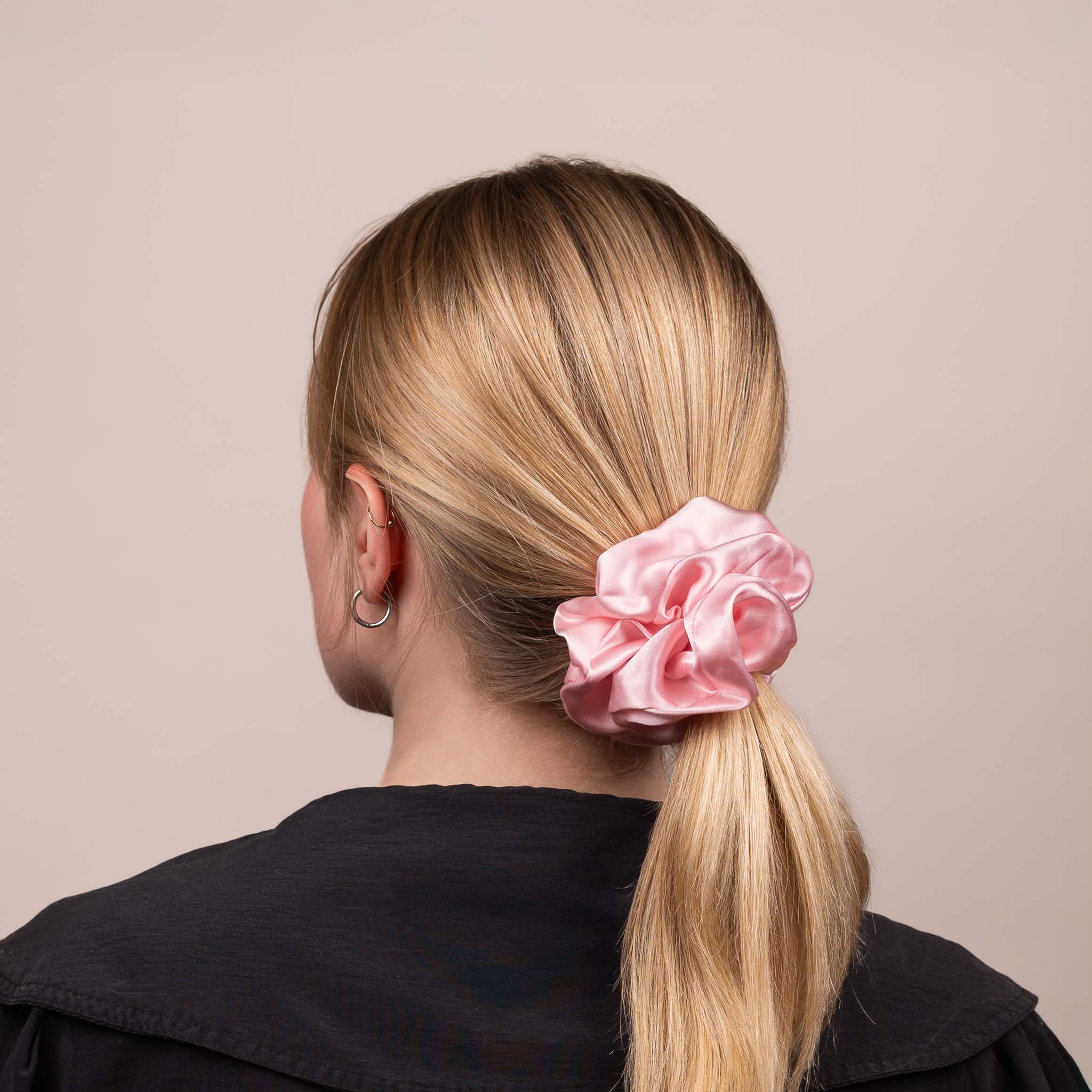 Side view of the Large Silk Scrunchie in Peony Pink securing hair in a low ponytail, with a soft sheen and drape.