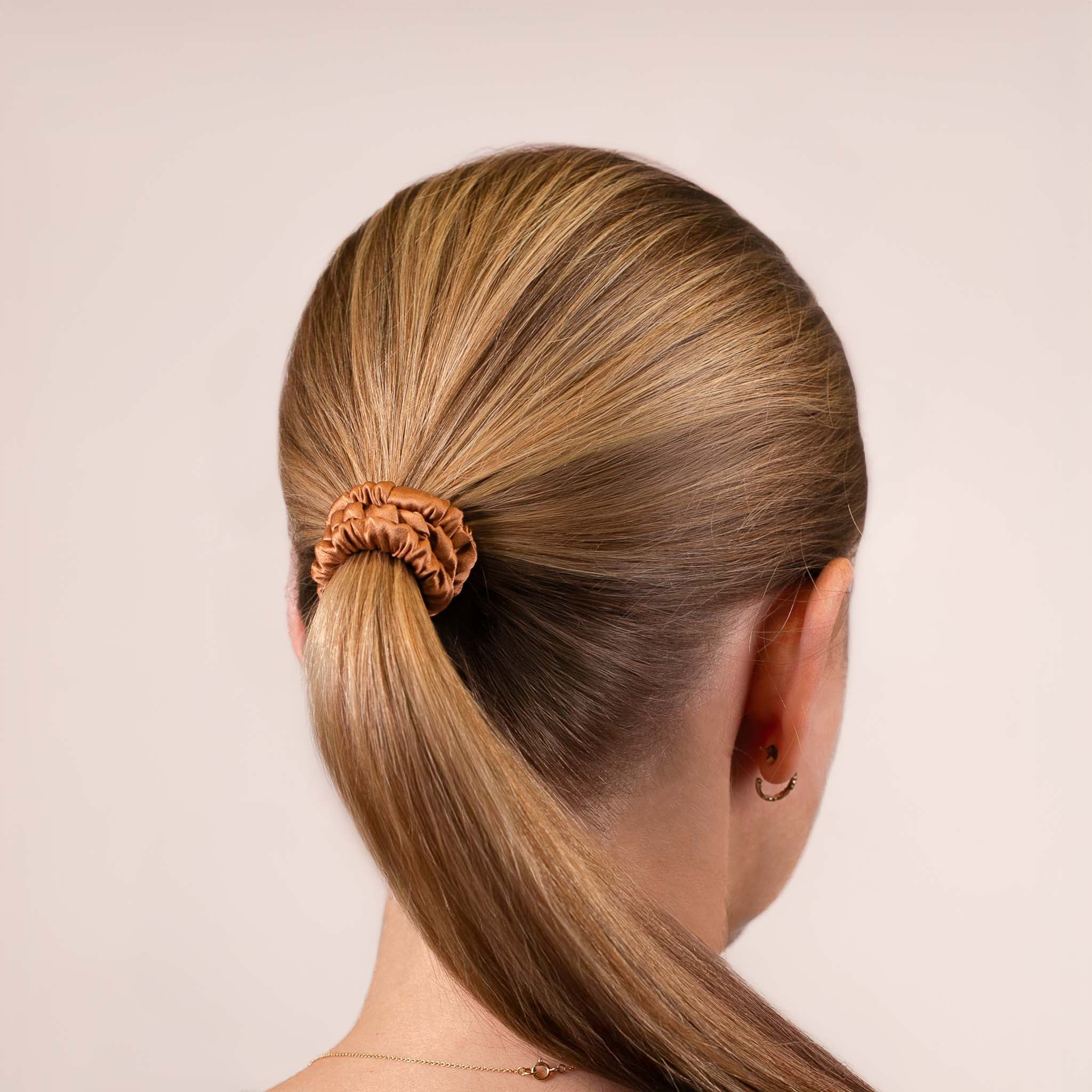 Skinny Silk Scrunchie in Caramel Brown securing a high ponytail, shown from the back, highlighting its smooth texture and soft sheen.