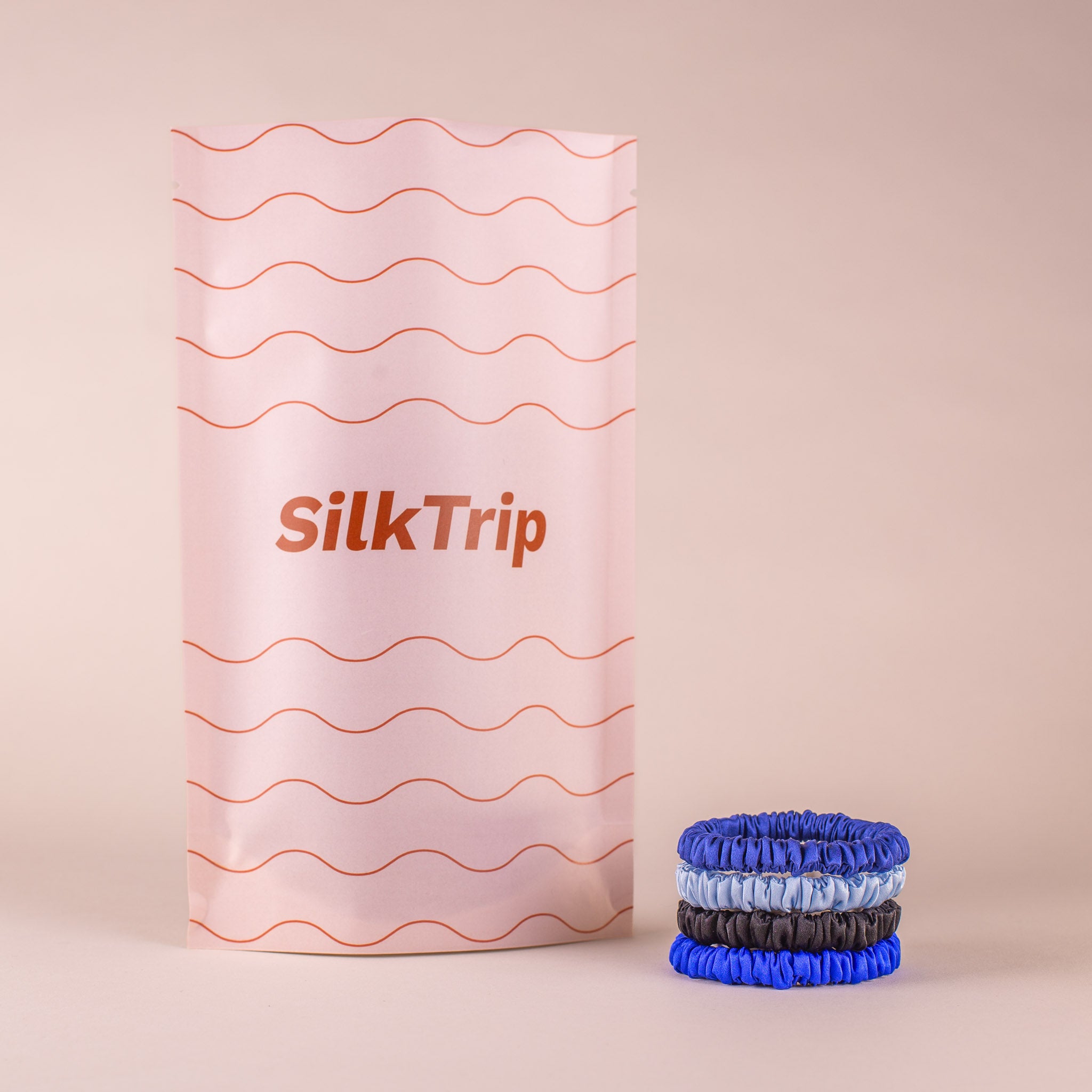Set of 4 Skinny Silk Scrunchies in Cool Headed, stacked beside SilkTrip’s soft-toned recycled paper packaging.