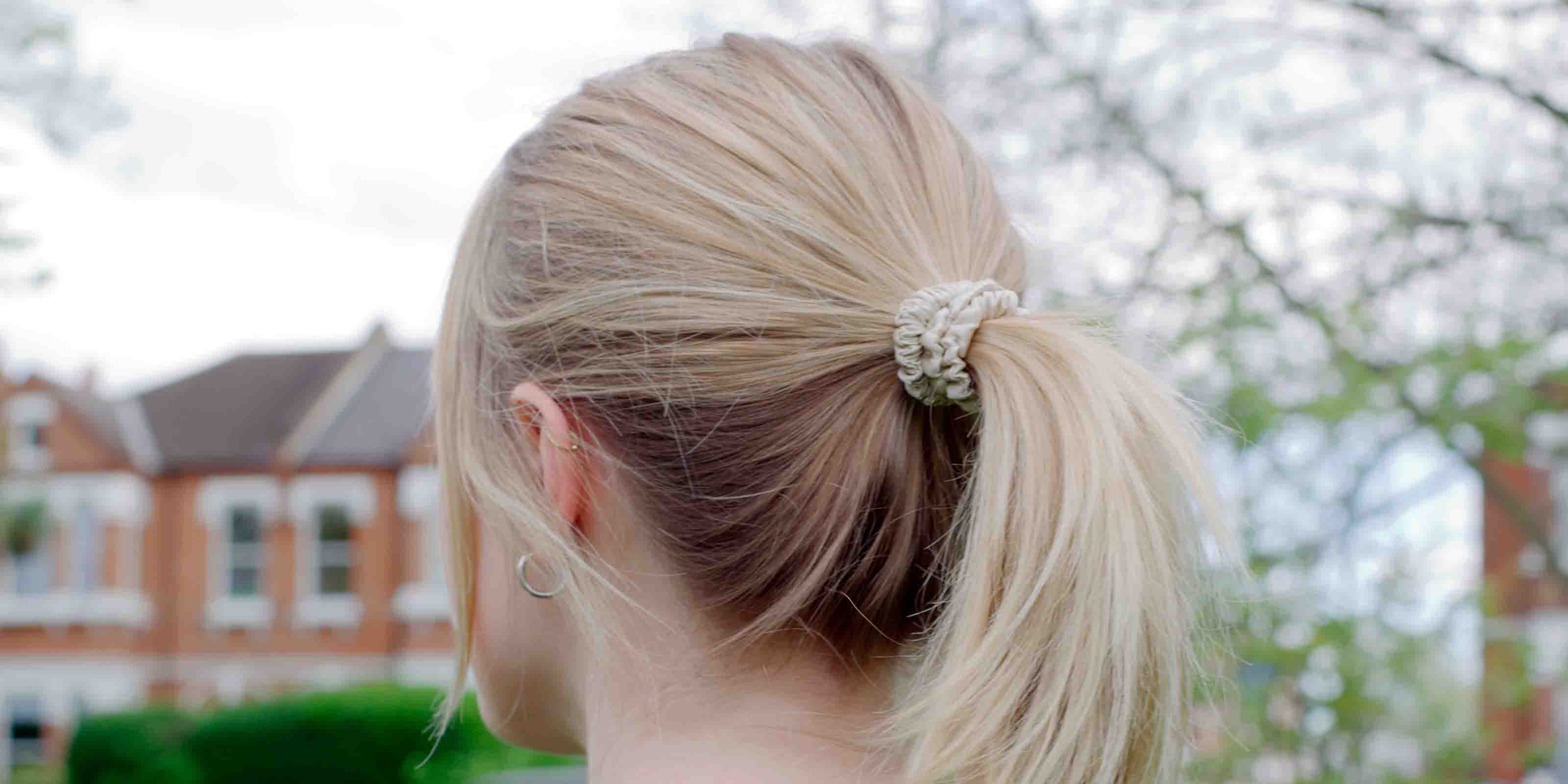A female wearing the Skinny Silk Scrunchie from SilkTrip in a high ponytail, before running in the park.