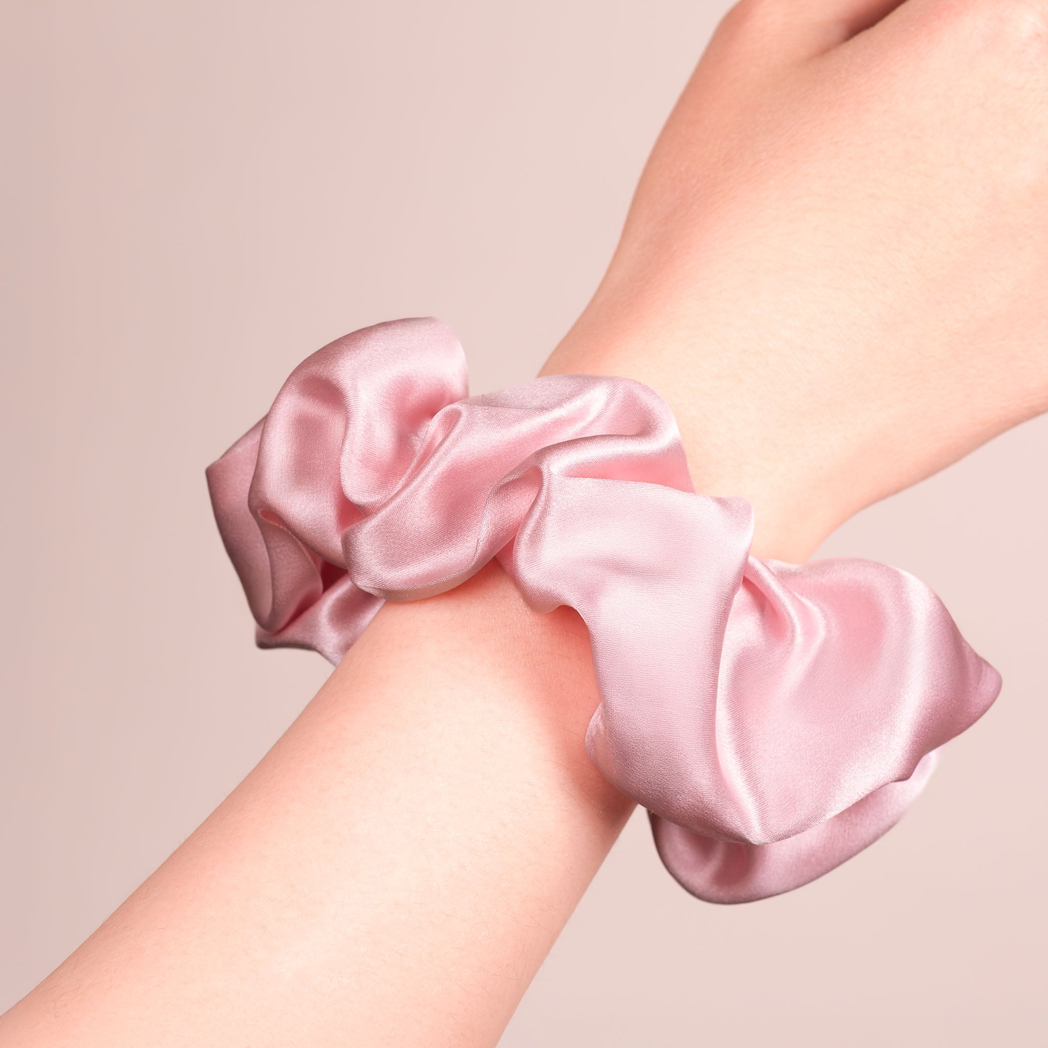 Large Silk Scrunchie in Peony Pink—a light peachy pink—worn on a wrist, showing a natural soft sheen and gentle drape.