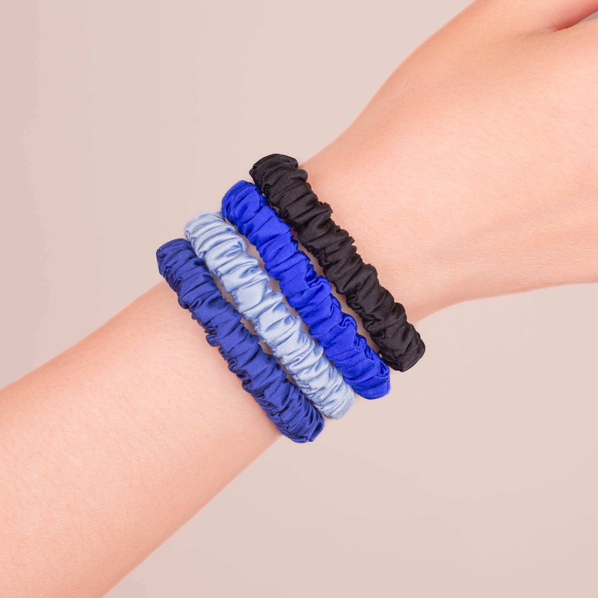 Set of 4 Skinny Silk Scrunchies in Cool-Headed, including Navy Blue, Icy Blue, Royal Blue, and Black—stacked on a wrist against a plain background.